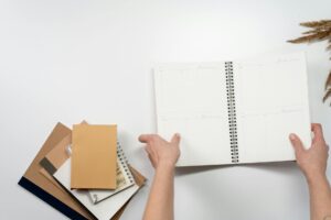 Flat lay of open notebook with minimalist office supplies and plant elements.